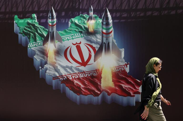 Photo of a woman walking in front of a mural that shows missiles being launched from Iran.