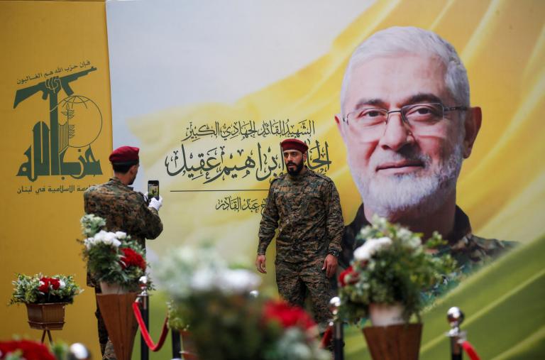 A Hezbollah fighter has his picture taken alongside a mural depicting deceased Hezbollah military leader Ibrahim Aqil at Aquil's funeral in September 2024 - source: Reuters