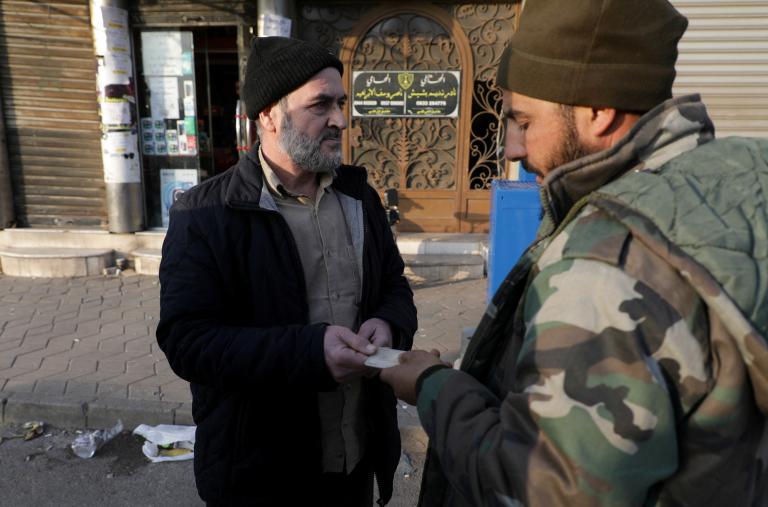 A fighter from Syria's de-facto post-Assad government checks a civilian's identity documents after a curfew was imposed in the Alawite-majority city of Homs in December 2024 - source: Reuters