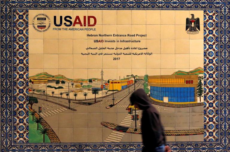 A local resident walks in front of a sign promoting a USAID-funded project in Hebron - source: Reuters