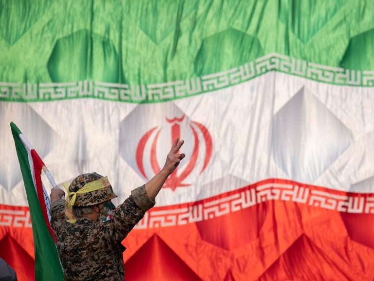 An Iranian soldier wearing an IRGC uniform salutes in front of an Iranin flag - source: Reuters