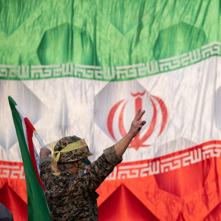 An Iranian soldier wearing an IRGC uniform salutes in front of an Iranin flag - source: Reuters