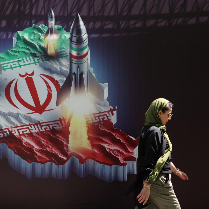 Photo of a woman walking in front of a mural that shows missiles being launched from Iran.