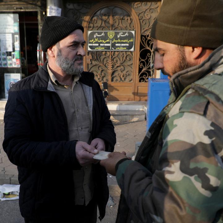 A fighter from Syria's de-facto post-Assad government checks a civilian's identity documents after a curfew was imposed in the Alawite-majority city of Homs in December 2024 - source: Reuters