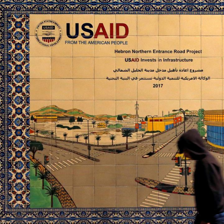 A local resident walks in front of a sign promoting a USAID-funded project in Hebron - source: Reuters