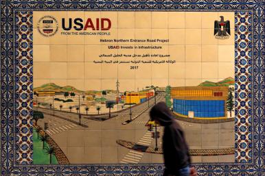 A local resident walks in front of a sign promoting a USAID-funded project in Hebron - source: Reuters